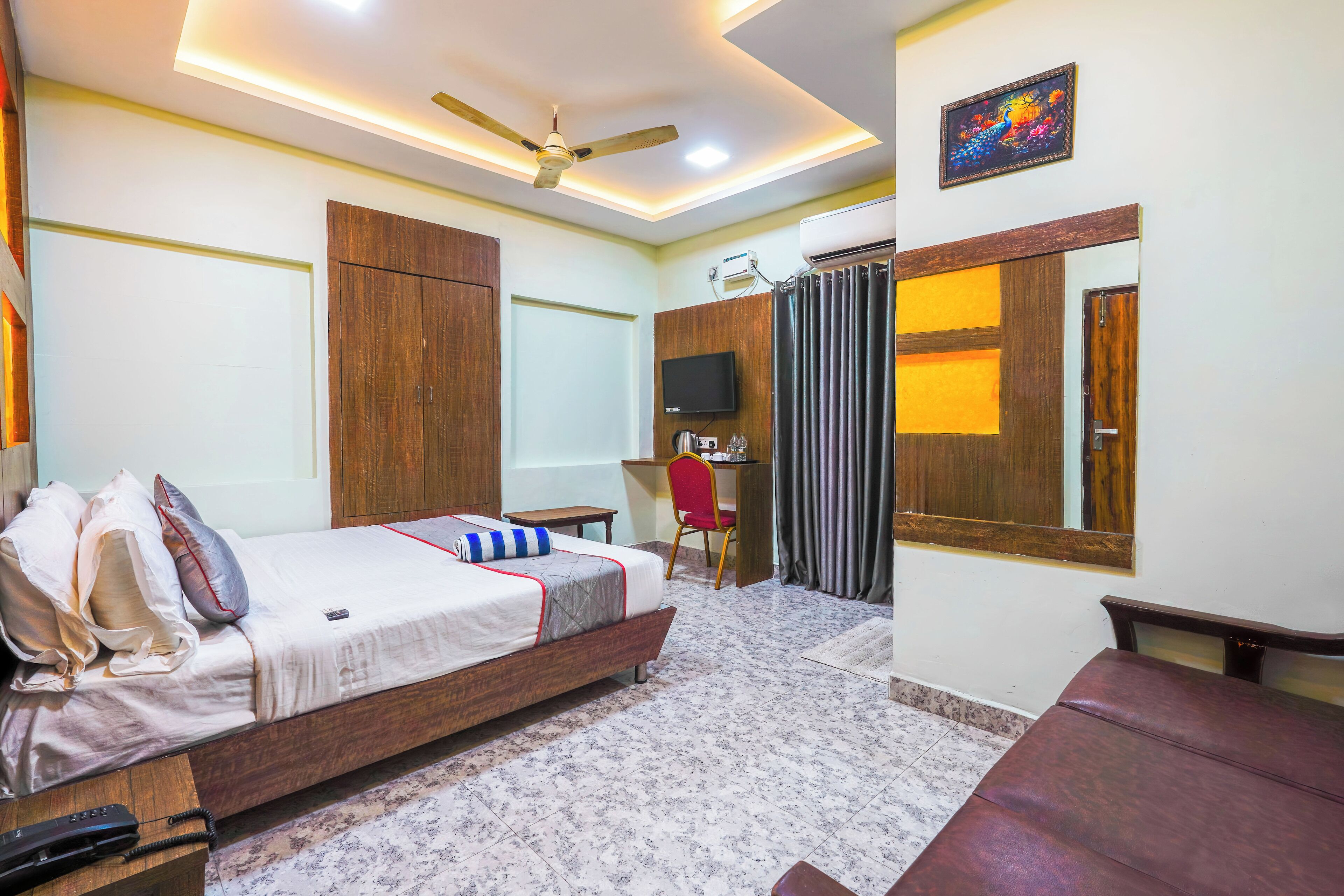 A hotel room with a bed, a desk, a chair, a ceiling fan, and a TV.