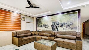 A modern living room with a sectional sofa, a glass coffee table, and a mural of elephants on the wall. - The K11 Hotels (Chennai)