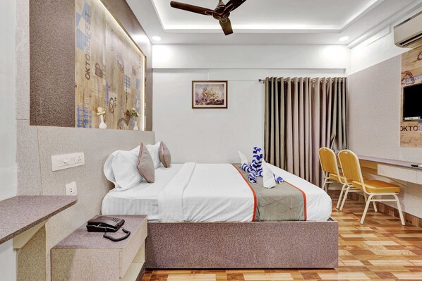 A hotel room with a bed, bedside table, desk, chairs, and a ceiling fan.