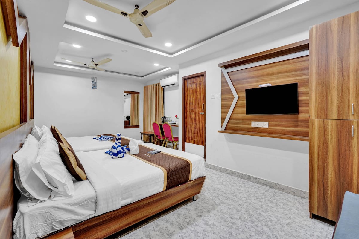 A hotel room with a bed, a desk, a chair, a TV mounted on the wall, and a wardrobe.