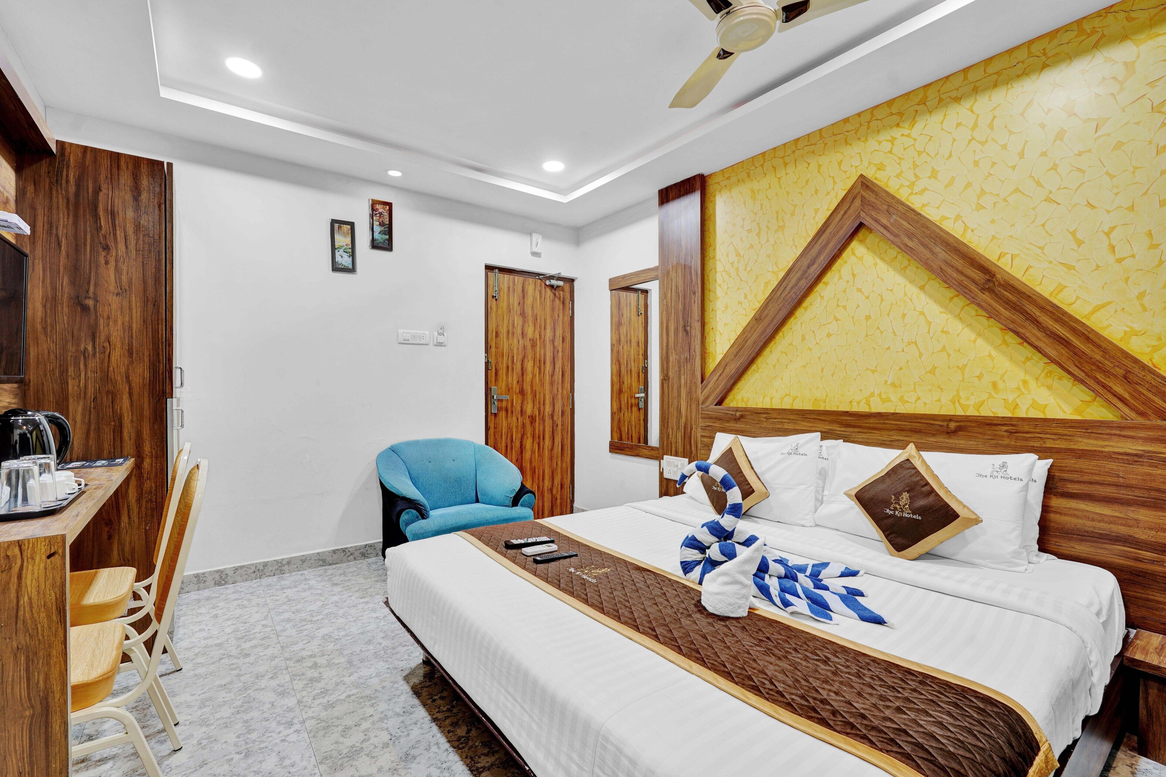 A hotel room with a bed, a desk with a chair, a ceiling fan, and wooden walls.