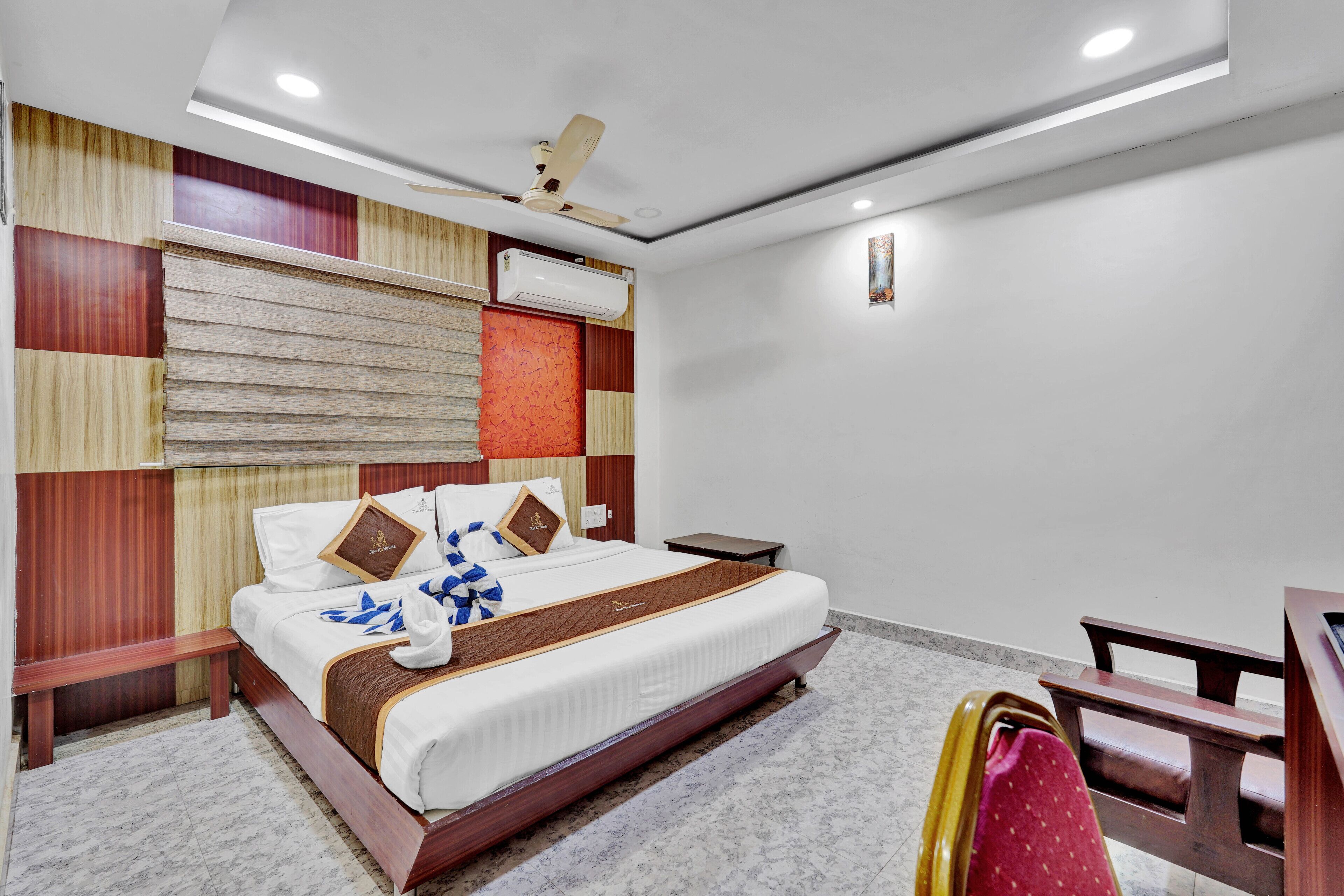 A hotel room with a bed, a desk, a chair, a ceiling fan, an air conditioning unit, and a wall-mounted light.