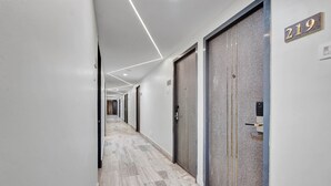 A hallway with a marble floor, numbered doors, and a modern light fixture. - The K11 Hotels (Chennai)