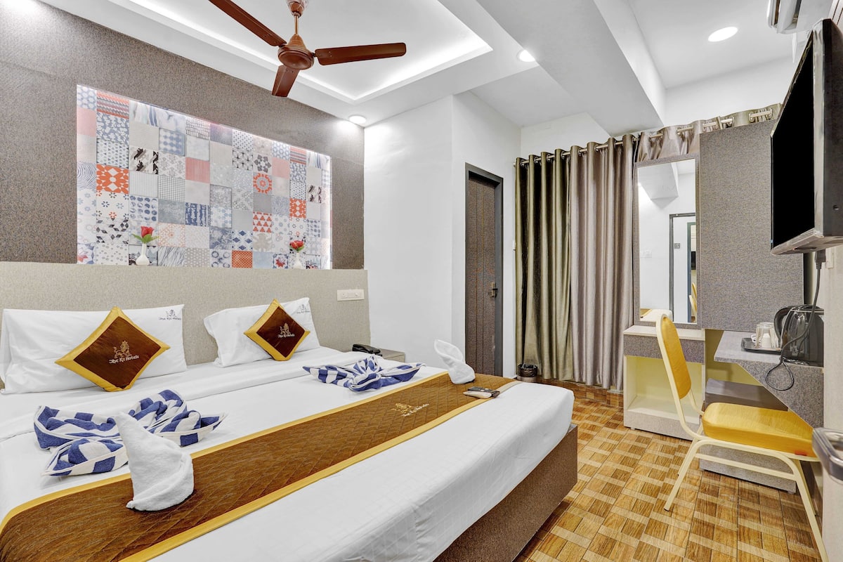 A hotel room with a large bed, a desk, a chair, and a television.