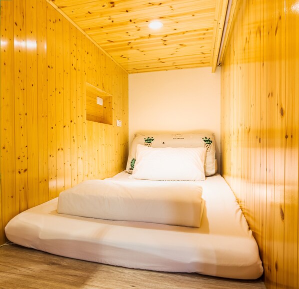 A wooden room with a bed, a shelf, and a wall socket.
