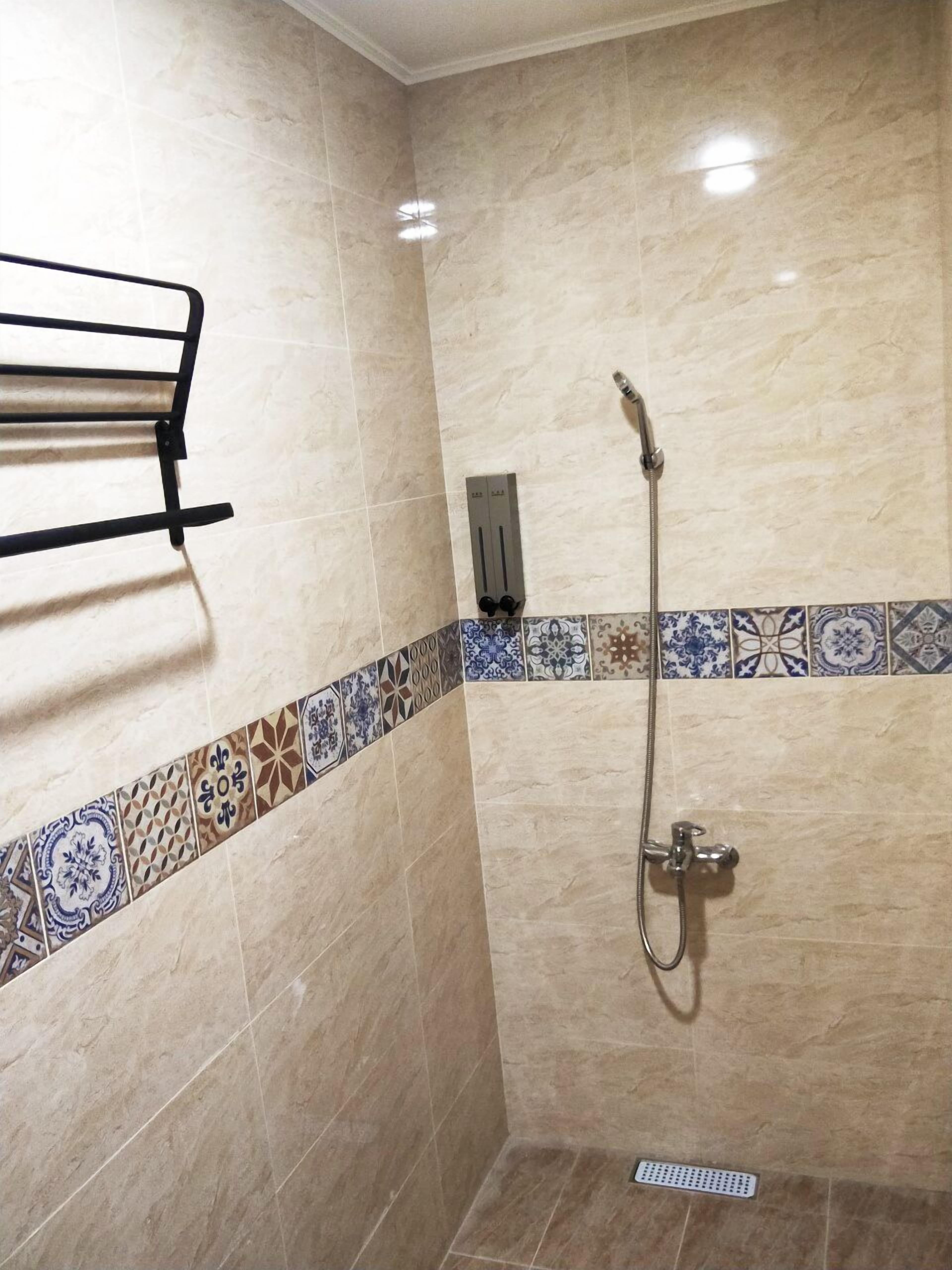 A shower area with a tiled wall, a towel rack, and a showerhead.