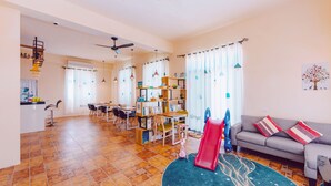 A spacious living area with a dining table, chairs, a sofa, a bookshelf, and a play area with a slide. - Hello Inn - Hostel (Magong)