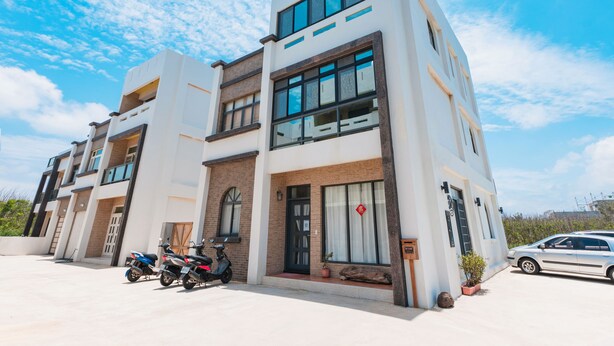 A modern multi-story building with a flat roof, large windows, and a parking area with scooters and a car. - Hello Inn - Hostel (Magong)