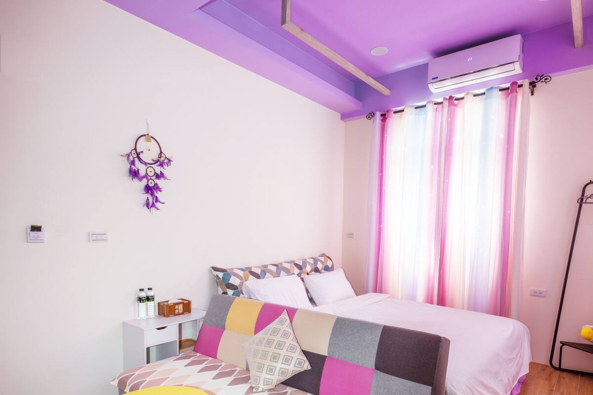 A bedroom with a bed, a bedside table, a small yellow table, and a wall-mounted air conditioner.