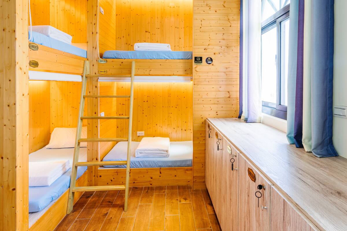 A wooden cabin with bunk beds, a ladder, a window with curtains, and a wooden cabinet.