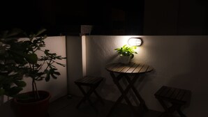A small outdoor seating area with a round table and two chairs, a potted plant, and a wall-mounted light fixture. - Hello Inn - Hostel (Magong)