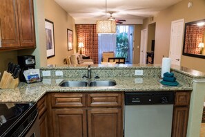 A kitchen with granite countertops, a built-in dishwasher, wooden cabinets, and a coffee maker. - Orlando | Family Theme Park Retreat | Pool + Hot Tub | 2BR (Orlando)