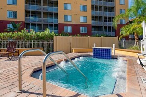 Une piscine avec un jacuzzi, entourée d’une terrasse en briques et bordée d’une clôture en bois.