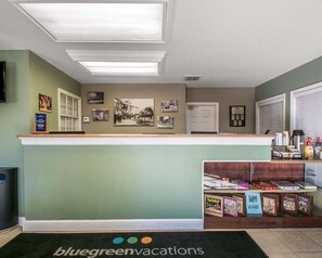 A reception area with a counter, framed pictures on the wall, and a shelf with books and toiletries.