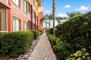A pathway flanked by neatly trimmed hedges and a building with multiple windows and balconies. - Orlando | Family Theme Park Retreat | Pool + Hot Tub | 2BR (Orlando)
