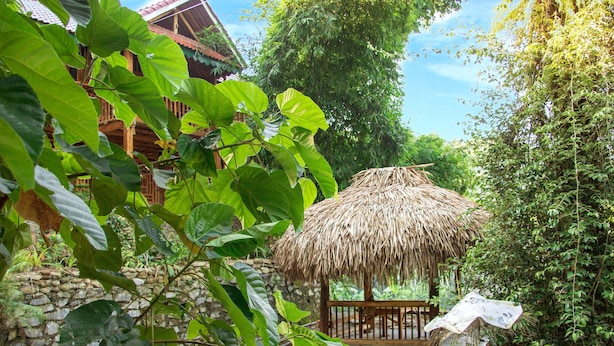 A thatched-roof hut with a wooden deck, surrounded by lush greenery and a stone wall. - I am a local guide,so i can provide the  information tour in my province for you (Ha Giang city)