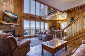 Un salón espacioso con chimenea, asientos cómodos, un televisor grande y vistas a las montañas a través de amplias ventanas.