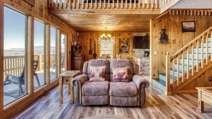 Un intérieur chaleureux en bois, avec un canapé, de grandes fenêtres, un lustre et un escalier.