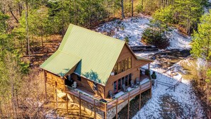 Une cabane en bois avec un toit vert, une terrasse et une vue sur une zone boisée.