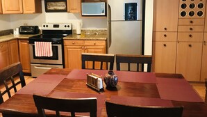 Una cucina con mobili in legno, un frigorifero in acciaio inossidabile, un forno a microonde, un fornello e un tavolo da pranzo con sedie.
