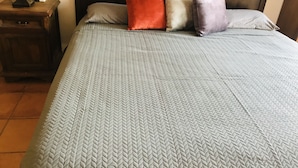 Un letto con una coperta trapuntata grigia e quattro cuscini nei colori rosso, bianco e viola.