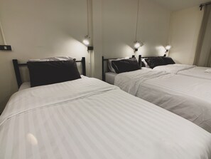 Two single beds with white bedding and dark pillows, each with a bedside lamp. - House 116 (Bangkok)