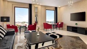 Een moderne woonkamer met een bank, rode stoelen, een salontafel en een grote televisie.
