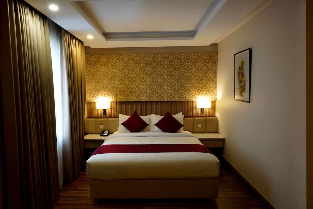 A hotel room with a large bed, two bedside tables with lamps, a patterned ceiling, and a framed picture on the wall.