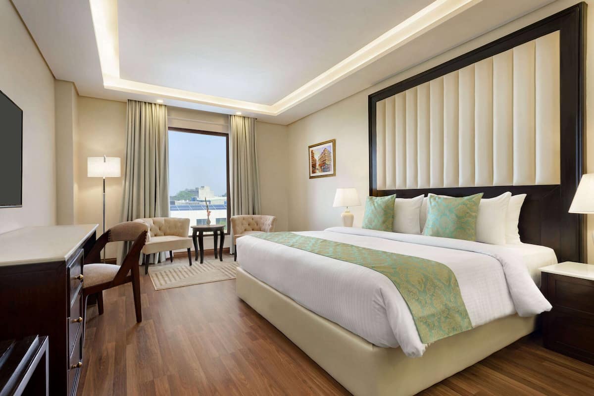 A hotel room with a large bed, a desk, a chair, and a view of the city.