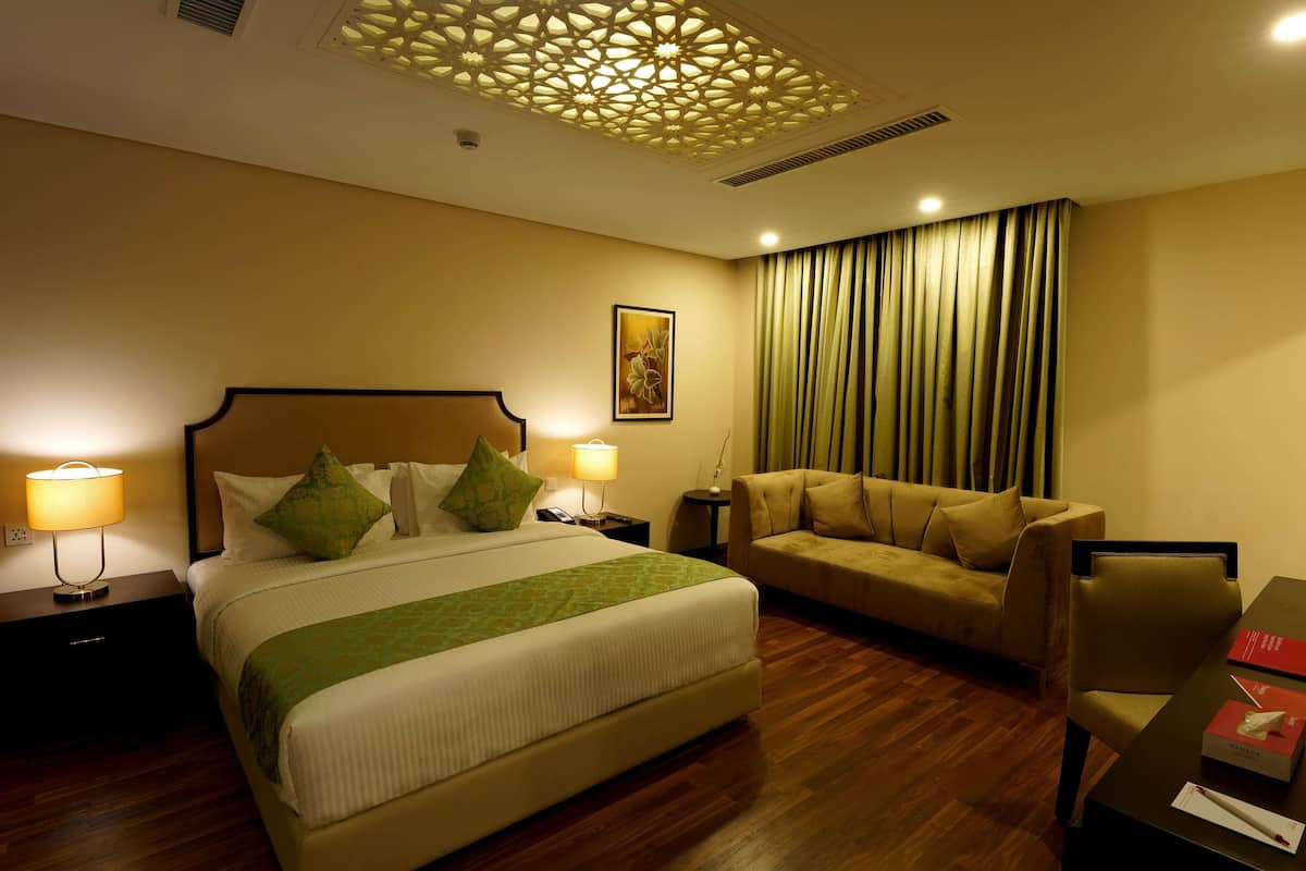 A hotel room with a large bed, a sofa, a desk, and a decorative ceiling.