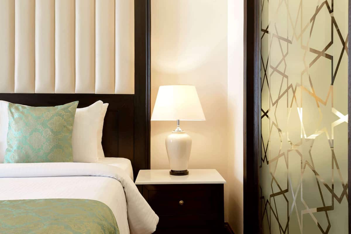 A neatly made bed with a white and teal bedspread, a white pillow, and a bedside table with a white lamp.
