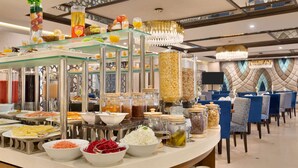 Een buffetopstelling met diverse etenswaren en drankjes, waaronder fruit, ontbijtgranen en sauzen.