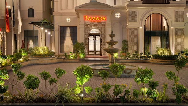 Een hotelentree met een bord waarop 'RAMADA' staat en een traditionele fontein in de binnentuin.