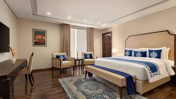 A hotel room with a large bed, a desk, a chair, a TV, and a painting on the wall.