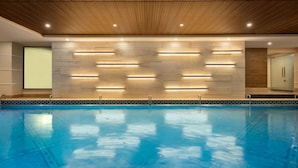 Een zwembad met een houten plafond en een betegelde wand met ingebouwde verlichting.