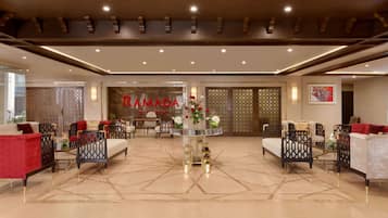 A spacious lobby with a central seating area, a decorative wall with the word "RAMADA" and a floral arrangement.