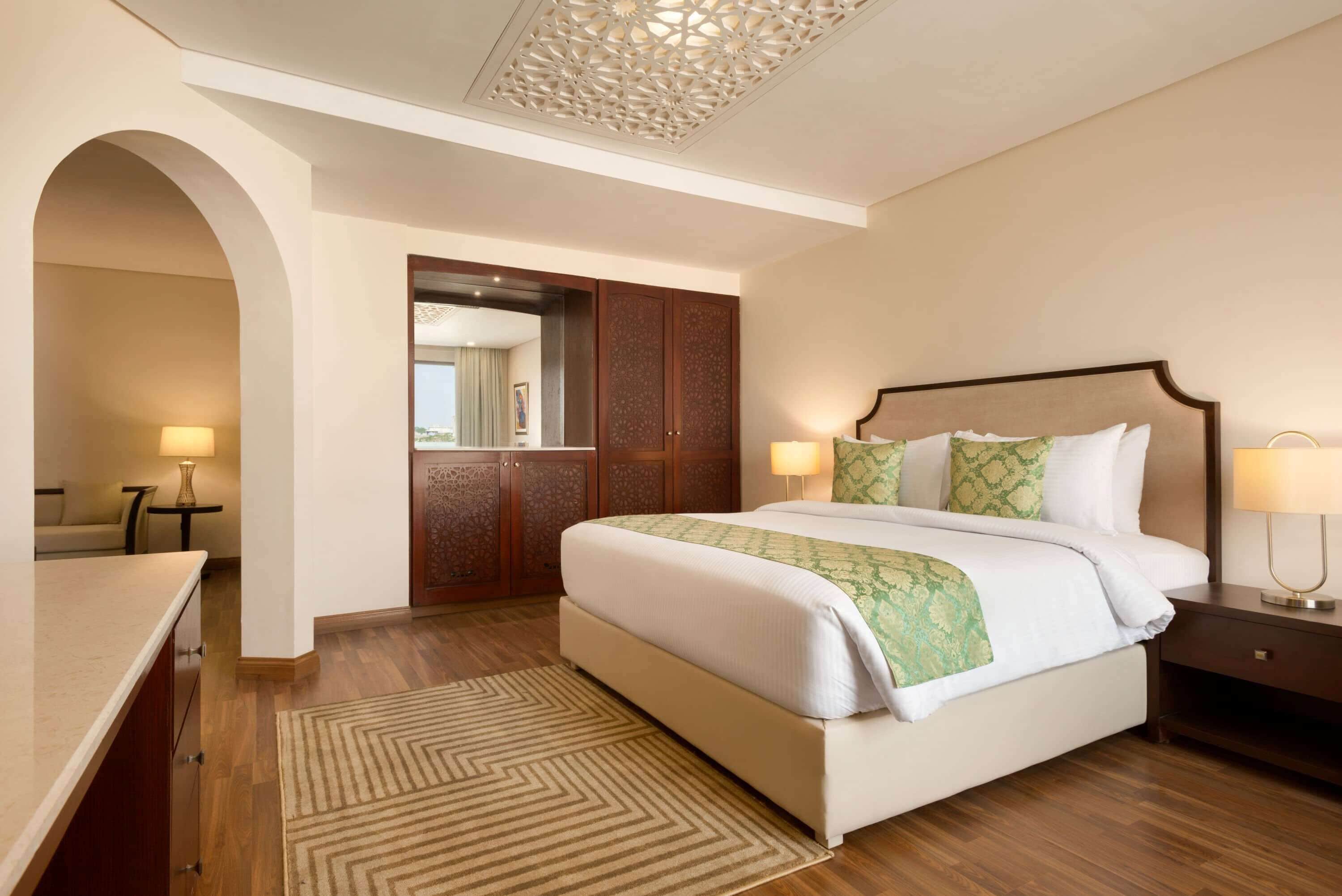 A hotel room with a large bed, a desk, and a wardrobe.