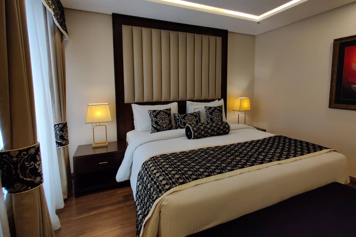 A hotel room with a large bed, two bedside tables, a headboard, and a nightstand.