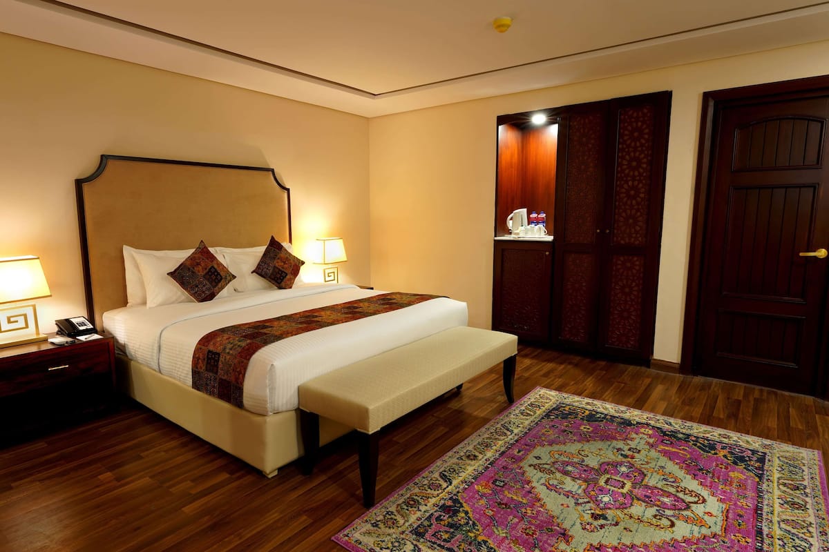 A hotel room with a large bed, bedside tables, a bench, a wooden floor, and a patterned rug.