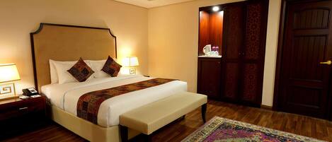 A hotel room with a large bed, bedside tables, a bench, a wooden floor, and a patterned rug.