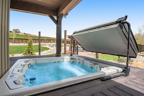 A hot tub with a wooden deck and a view of a backyard.