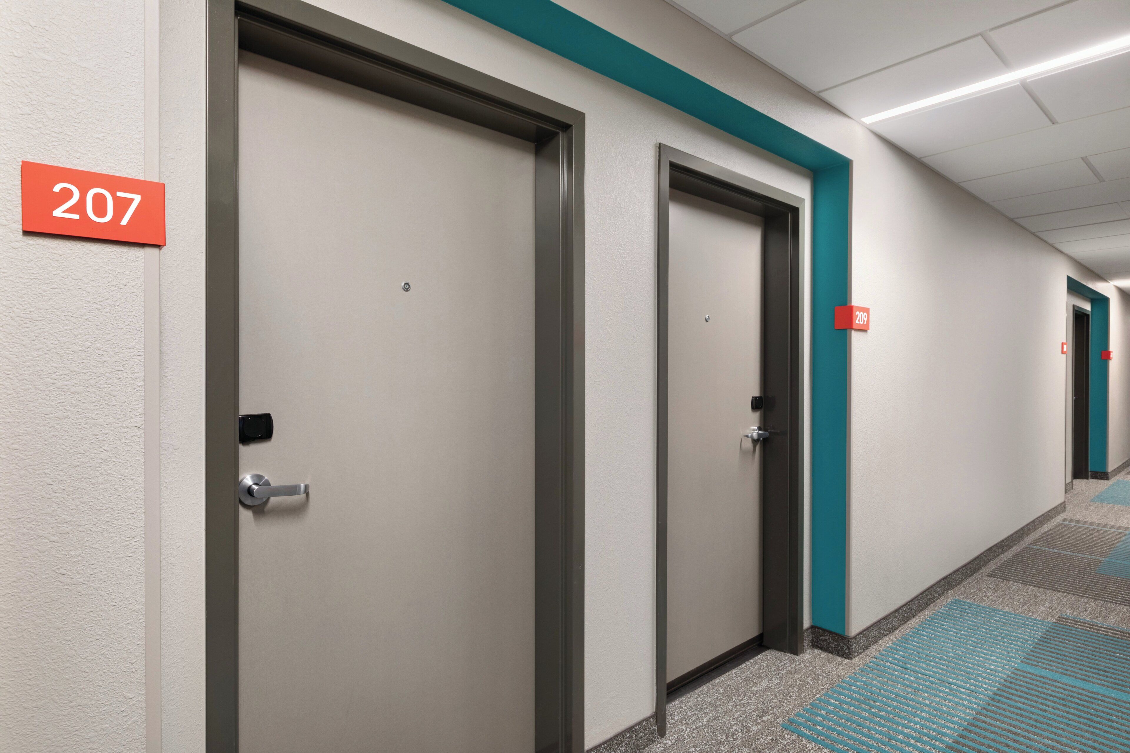 A hallway with doors numbered 207 and 209, carpeted floor, and a teal accent wall.