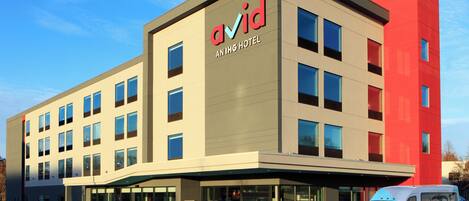 A modern building with the name 'Avid Anling Hotel' on the facade, featuring a flat roof, multiple windows, and a parking area with a van.