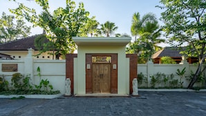 A gated entrance with a wooden door, surrounded by a low wall and greenery. - Benian Villas (Nusa Dua)