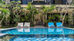 A swimming pool with checkered tiles, surrounded by palm trees and lounge chairs. - Benian Villas (Nusa Dua)
