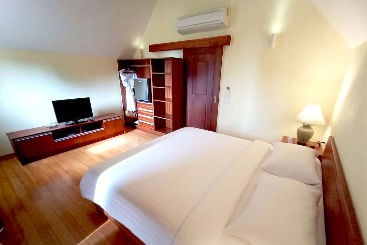 A hotel room with a large bed, a TV on a wooden cabinet, a wardrobe, and a bedside lamp.