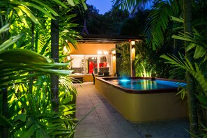 Una piscina con zona cubierta, rodeada de abundante vegetación.