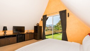 Ett sovrum med en stor säng, en tv, en minibar och utsikt över ett grönområde.