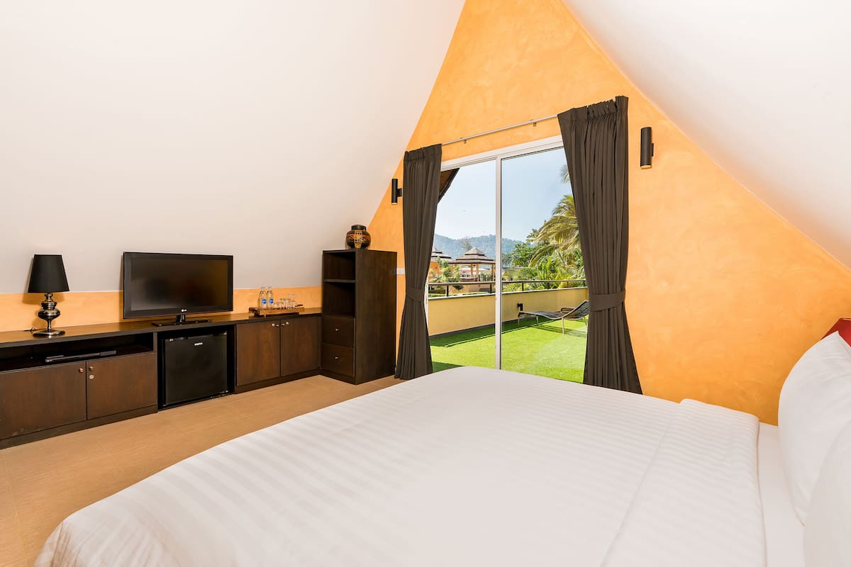A bedroom with a large bed, a television, a minibar, and a view of a green outdoor area.