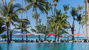 A poolside area with lounge chairs and umbrellas, surrounded by palm trees and overlooking a body of water.